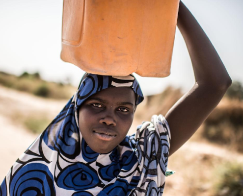 Lubabatu* , 13, walks home after collecting water from a Save the Children water point in the informal displacement camp at Musari, outside Maiduguri. Image credit: Tommy Trenchard / Save the Children
