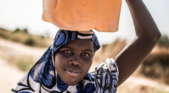 Lubabatu* , 13, walks home after collecting water from a Save the Children water point in the informal displacement camp at Musari, outside Maiduguri. Image credit: Tommy Trenchard / Save the Children