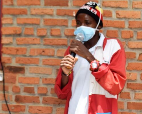 Save the Children health worker Ahishakiye delivers COVID-19 prevention messages to families waiting outside a clinic. Image credit: Thacien Biziyaremye / Save the Children